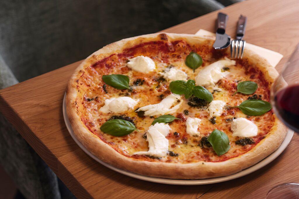 Eine köstliche Pizza mit frischer Burrata und Basilikum auf einem Holztisch.
